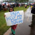 A woman holds a banner written "Papa Help My Country Burundi" before a mass by Pope Francis, as rain falls in Kenya"s capital Nairobi, November 26, 2015.
