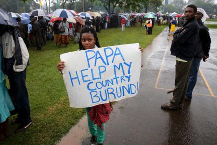 A woman holds a banner written "Papa Help My Country Burundi" before a mass by Pope Francis, as rain falls in Kenya"s capital Nairobi, November 26, 2015.