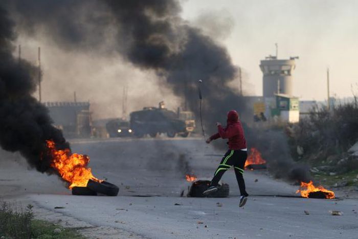 A Palestinian protester uses a sling to hurl stones towards Israeli troops during clashes, near Israel's Ofer Prison near the West Bank city of Ramallah December 25, 2015.