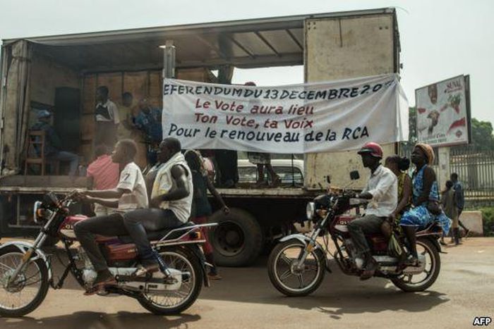 Motorbikes past an electoral caravan with a banner that reads, "The vote will take place, your vote, your voice," in Bangui, Central African Republic.