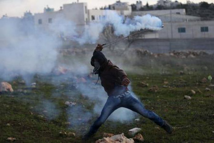 A Palestinian protester returns a tear gas canister fired by Israeli troops during clashes in the West Bank village of Silwad, near Ramallah December 26, 2015.