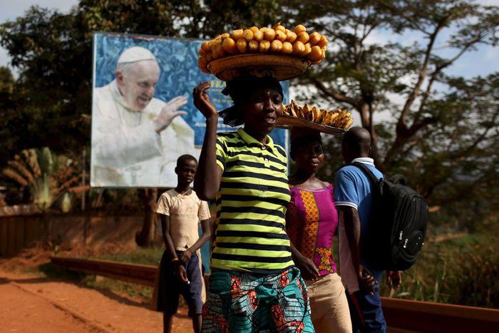 Women carrying fruits and vegetables on their heads walk past a billboard with a photograph of Pope Francis, in Bangui, Central African Republic, November 26, 2015. REUTERS/Siegfried Modola