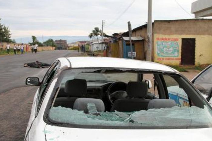 A car damaged by gunfire is seen abandoned as residents walk past bodies of unidentified men killed during gunfire, in the Nyakabiga neighbourhood of Burundi"s capital Bujumbura, December 12, 2015.