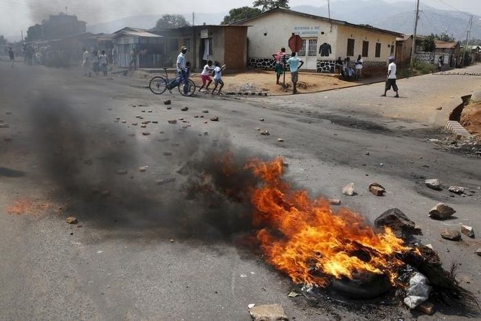Residents move past a burning barricade on a rock strewn street in Bujumbura's Niyakabiga district on Presidential election day in Burundi, July 21, 2015. REUTERS/Mike Hutchings