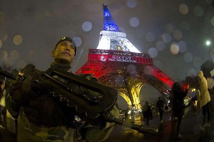 A French soldier in front of the Eiffel Tower, which is illuminated with the colours of the French national flag.