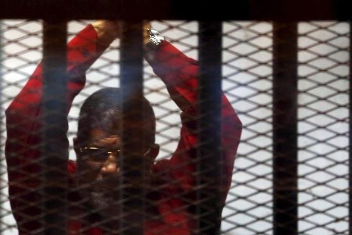 Deposed President Mohamed Mursi greets his lawyers and people from behind bars at a court wearing the red uniform of a prisoner sentenced to death, during his court appearance with Muslim Brotherhood members on the outskirts of Cairo, Egypt, June 21, 2...