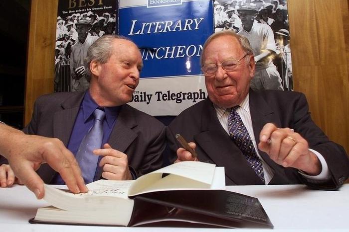Former Australian cricketing great Arthur Morris (R) signs books with Roland Perry, author of the book titled 'Bradman's Best', at the launch in Sydney August 13, 2001. DG/RCS/Files