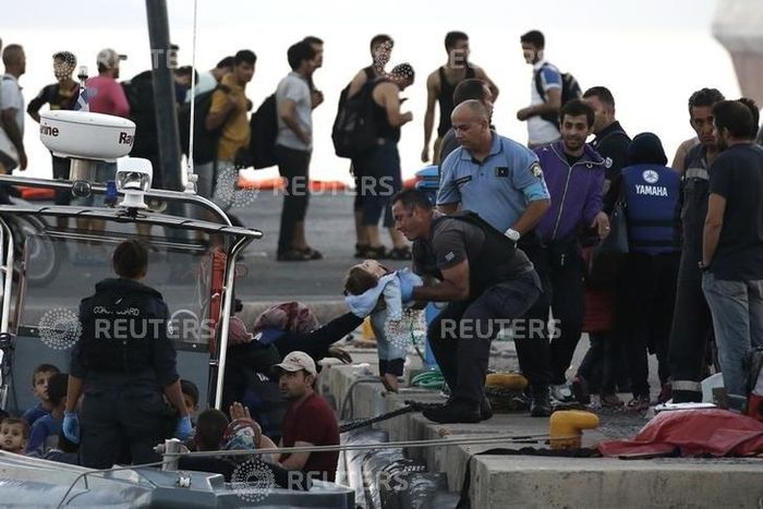 A migrant hands a baby to a Hellenic Coast Guard officer following a rescue operation, at the port on the Greek island of Kos, August 17, 2015. REUTERS/Alkis Konstantinidis