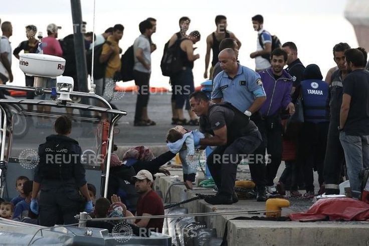 A migrant hands a baby to a Hellenic Coast Guard officer following a rescue operation, at the port on the Greek island of Kos, August 17, 2015. REUTERS/Alkis Konstantinidis