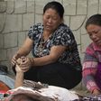 Grieving women hold the hands of relatives as they lie beneath a thin white sheet in the city of Kathmandu.