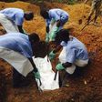 Volunteers lower a corpse, which is prepared with safe burial practices.
