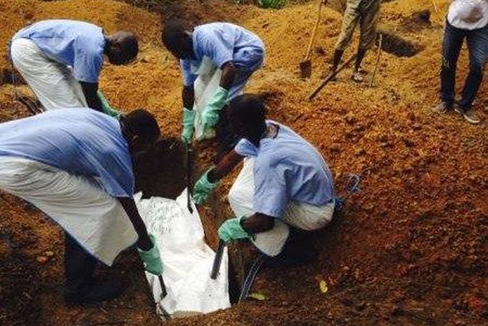 Volunteers lower a corpse, which is prepared with safe burial practices.