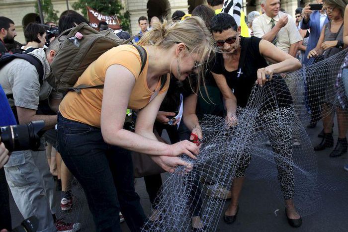 People cut a net that symbolises a fence, during a demonstration against a fence being built at the Hungarian-Serbian border, in Budapest, Hungary, July 14, 2015. REUTERS/Bernadett Szabo