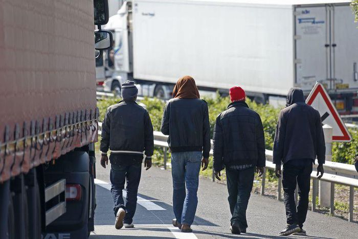 Migrants walk near trucks blocked on a road which leads to the Channel Tunnel terminal in Coquelles near Calais, northern France, July 1, 2015.    REUTERS/Vincent Kessler