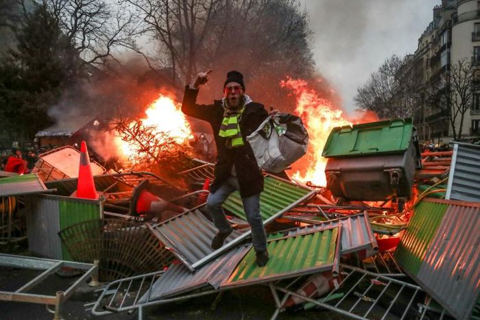 A yellow vest "Gilets Jaunes" anti-government protestor stands on a burning barricade in Paris on January 5 during clashes with security personnel