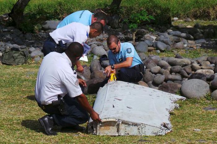 French gendarmes and police inspect a large piece of plane debris which was found on the beach in Saint-Andre, on the French Indian Ocean island of La Reunion, July 29, 2015.