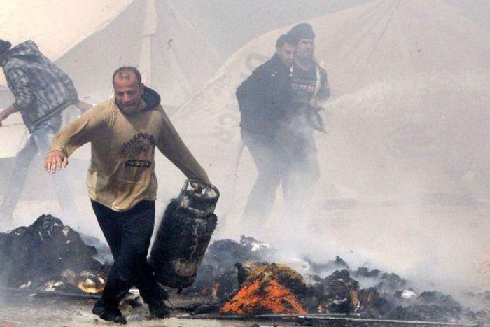 A Syrian refugee runs with a gas bottle cylinder, between burning tents.