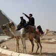 A police officer sitting on a camel talks to workers at the Giza pyramids, south of Cairo, February 20, 2014. REUTERS/Asmaa Waguih