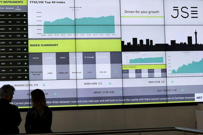People chat in front of an electronic board displaying movements in major indices at the Johannesburg Stock Exchange building in Sandton Johannesburg July 9, 2015.  REUTERS/Siphiwe Sibeko