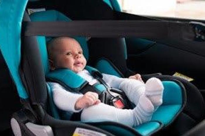 A baby strapped into a car seat, inside a car