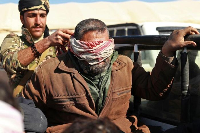 A suspected Islamic State (IS) group fighter who fled from the frontline Syrian village of Baghouz, near the Iraqi border, sits blindfolded in the back of a pickup truck after he was taken into custody by SDF forces for screening