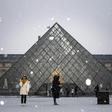 Tourists take pictures at the Louvre Pyramid as the snow falls over Paris