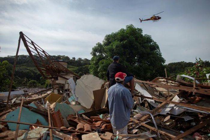 People look at a firefighter helicopter flying over the mud-hit area a day after the collapse of a dam at an iron-ore mine belonging to Brazil's giant mining company Vale near the town of Brumadinho, Brazil on January 26, 2019