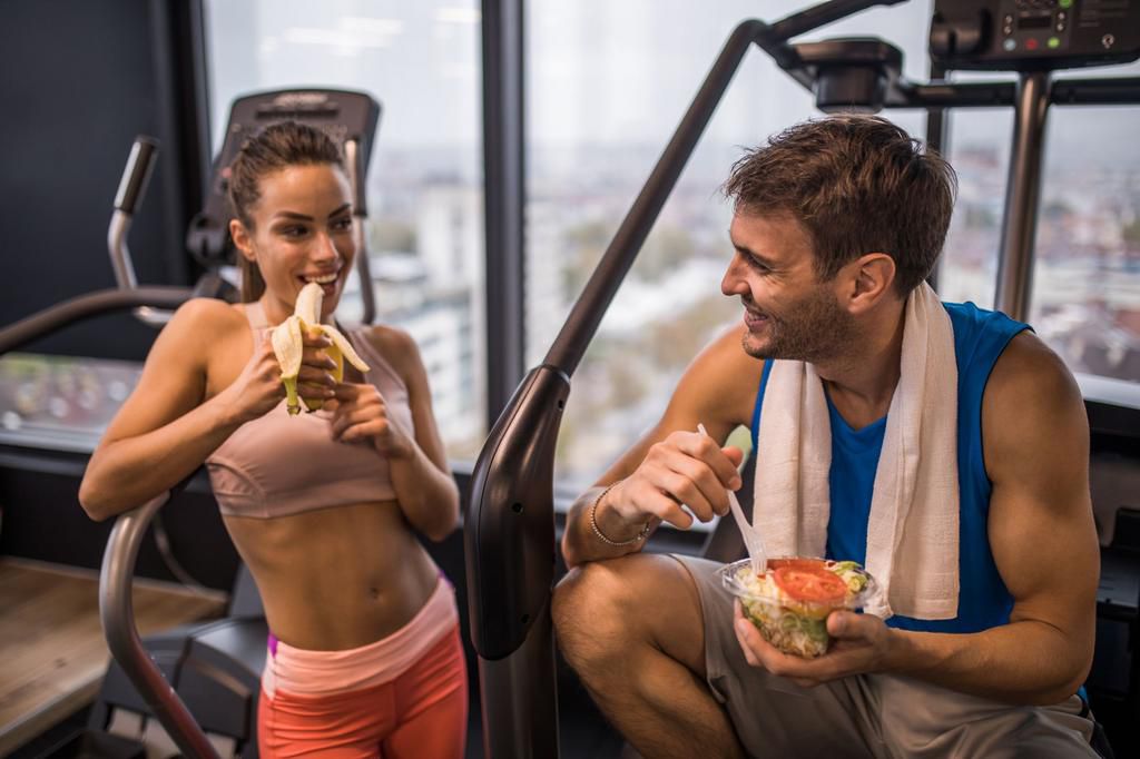 Happy athletic couple eating healthy food on a break in a gym.