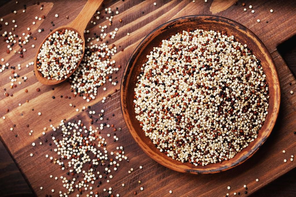 Mixed quinoa in bowl on wooden kitchen board top view.