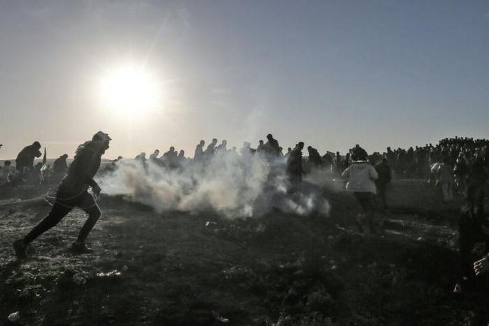 Palestinian protesters run through tear gas during clashes with Israeli forces following a demonstration at the border of the Gaza Strip on January 11, 2019