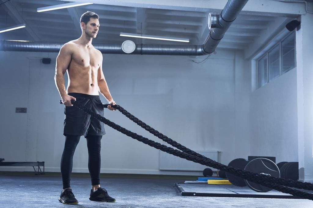 Athletic man exercising with battle ropes at gym