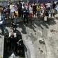 People collect water from a broken pipe flowing into a sewage canal at the Guaire river in Caracas on March 11, 2019