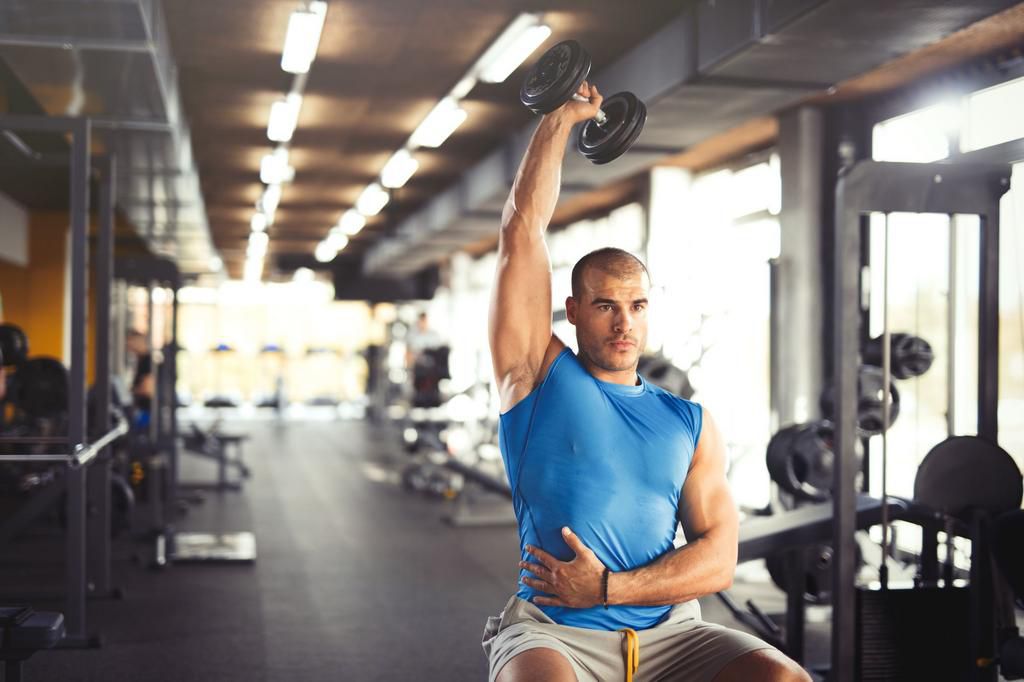 Young muscular man lifting up dumbbells at the gym.