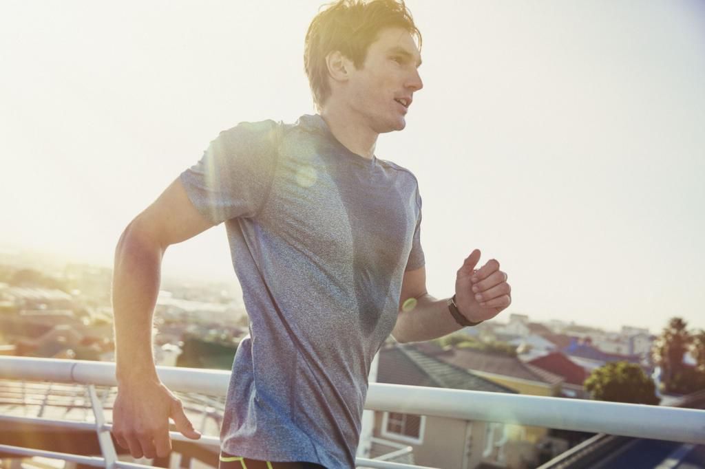 Sweaty male runner running on sunny urban footbridge at sunrise