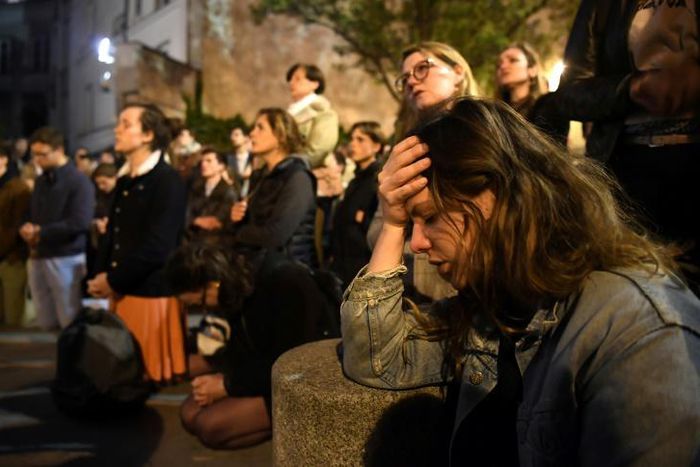 Onlookers react as they watch flames engulf Notre-Dame Cathedral in Paris on April 15, 2019