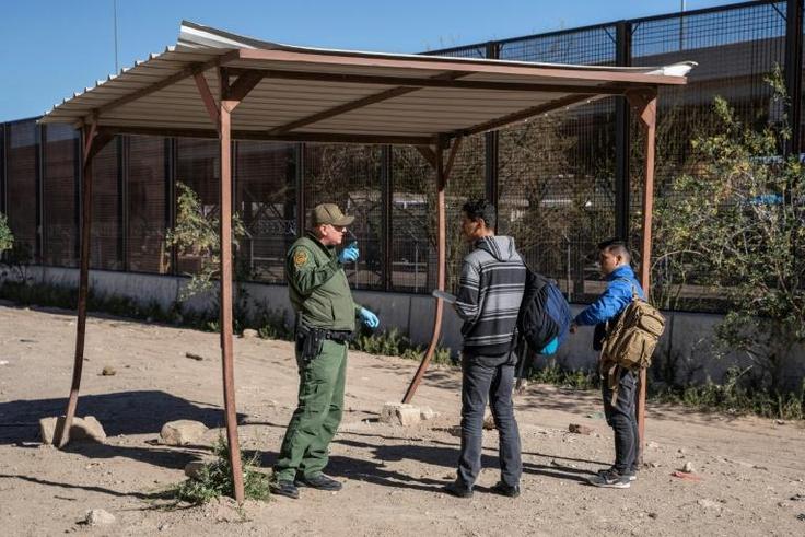 Salvadoran migrants speak with a member of the US border patrol by the border fence after crossing the Rio Grande to claim asylum