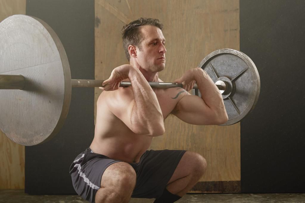 Mid adult male weightlifter lifting barbell in gym