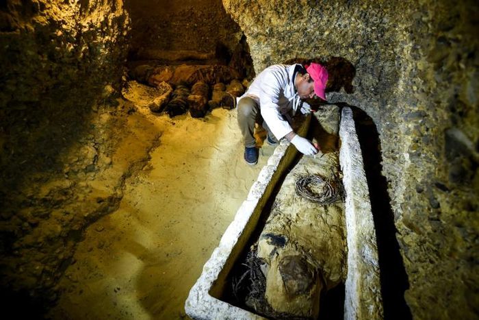 An archaeologist brushes a newly-discovered mummy laid inside a sarcophagus, part of a collection found in burial chambers dating to the Ptolemaic era (323-30 BC) in February 2019