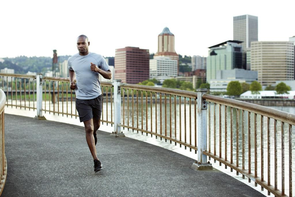 Confident male athlete running on footbridge over river against clear sky in city