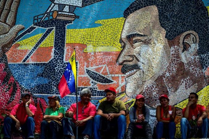 Supporters of Venezuelan President Nicolas Maduro sit backdropped by a mosaic depicting their leader, during a demonstration in Caracas on March 16, 2019