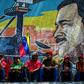 Supporters of Venezuelan President Nicolas Maduro sit backdropped by a mosaic depicting their leader, during a demonstration in Caracas on March 16, 2019