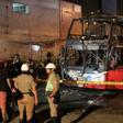Police stand around the charred remains of a bus that caught fire in Lima killing 20 people