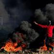 A Palestinian protester waves a flag near burning tyres during clashes with Israeli forces after a demonstration at the border with Israel, east of Gaza City