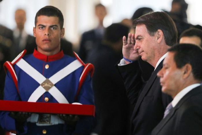 This file photo shows Brazilian President Jair Bolsonaro (saluting) as he and Vice President Hamilton Mourao receive a military award in Brasilia on March 28, 2019; Bolsonaro wants troops to mark the anniversary of a 1964 military coup