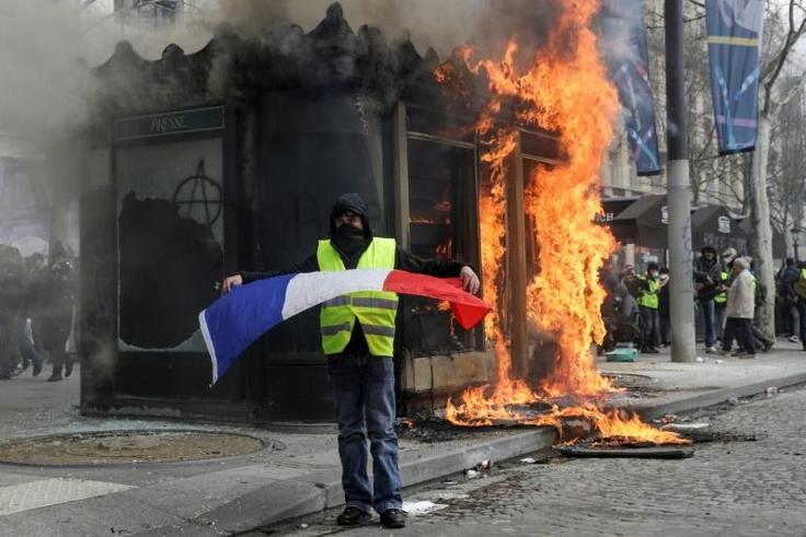 A Yellow Vest protester waves a French flag as fire rages on the Champs-Elysees on Saturday