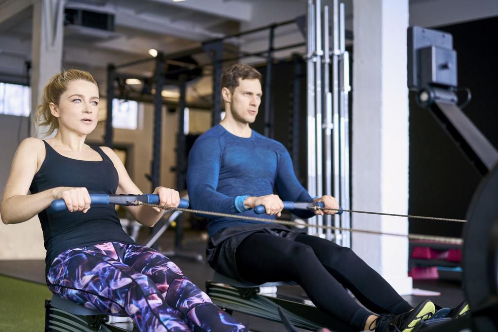 Man and woman at gym exercising together on rowing machines