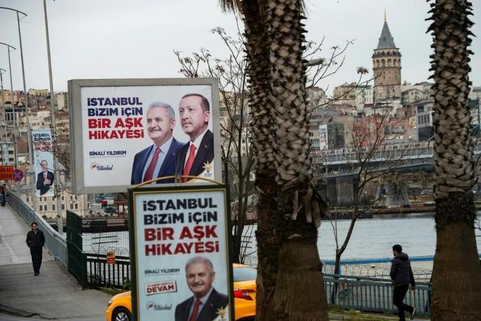 People walk past election banners of Turkish President Tayyip Erdogan and AK Party's mayoral candidate for Istanbul, Binali Yildirim, in Istanbul