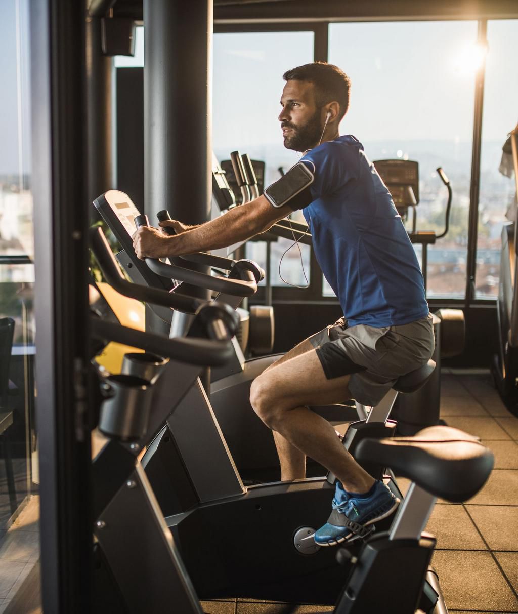 Young man listening music on exercise bike in a gym.