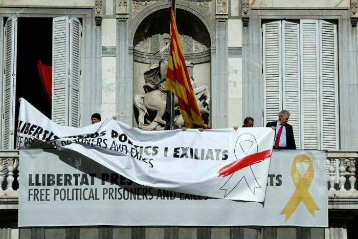 A banner reading "Free political prisoners and those exiled" bearing a white ribbon with a red brush stroke replaces an older one bearing a yellow ribbon on the balcony of the regional government's headquarters in Barcelona