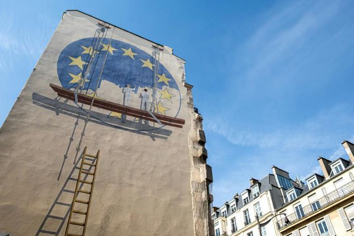 A trompe l'oeil shows two workers painting the European Union flag on the side of a building in Paris